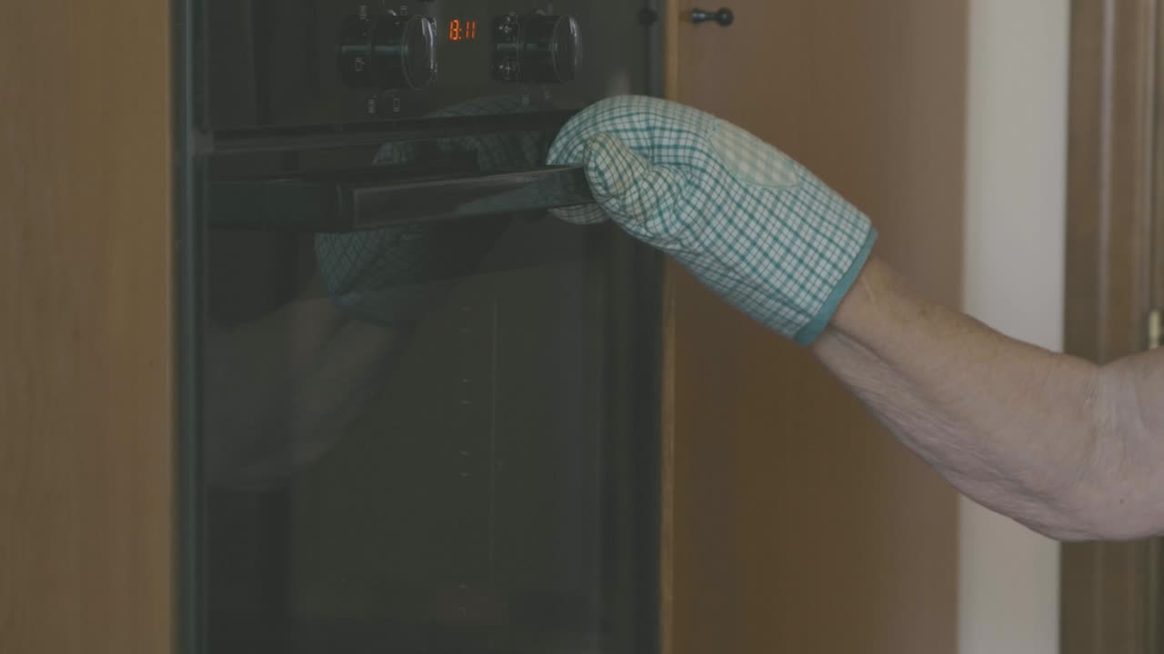 una anciana abre un horno con un guante para observar si el pastel está listo