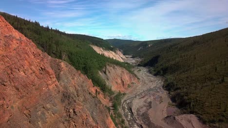 emocionante vuelo en el desierto abrazando la ladera de la montaña y el lecho de roca roja al lado del borde del acantilado en yukon burwash creek hacia el sensacional y majestuoso día azul del cielo soleado, canadá, enfoque aéreo