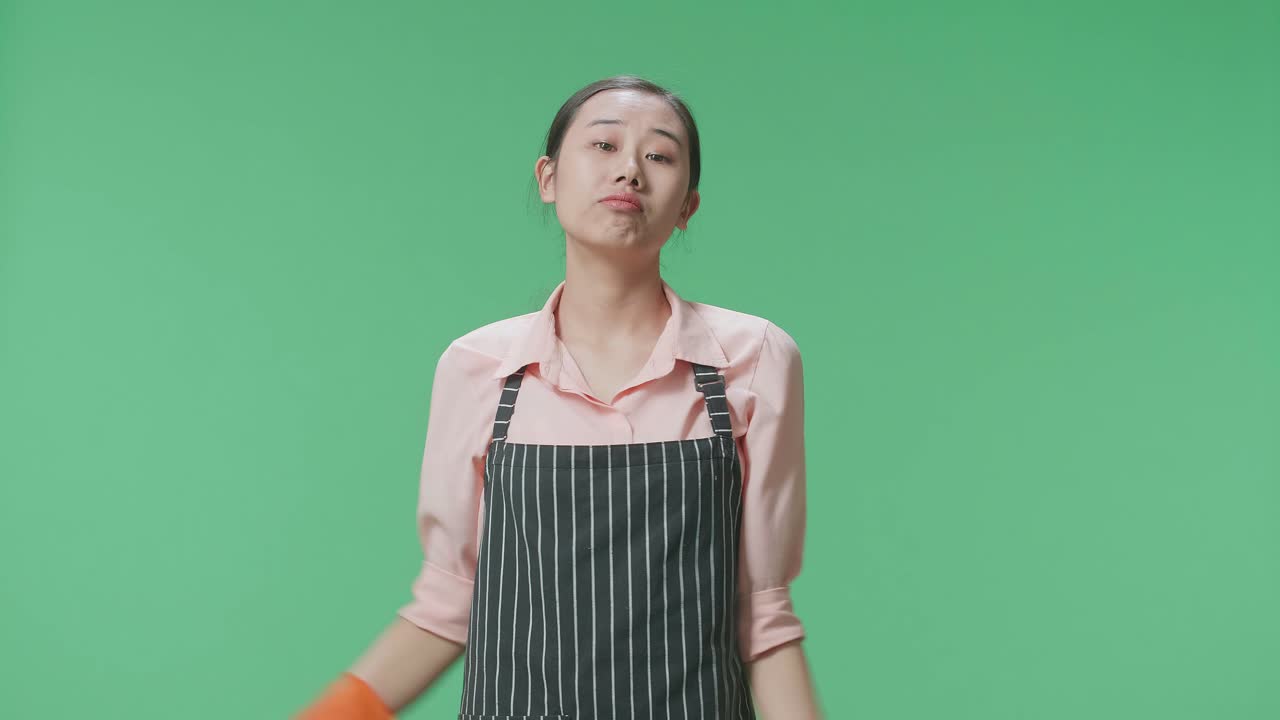 아시안 여성 집주인이 앞옷을 입고 스프레이와 부 스폰지를 버리고 녹색 스크린 스튜디오에서 팔을 교차합니다.