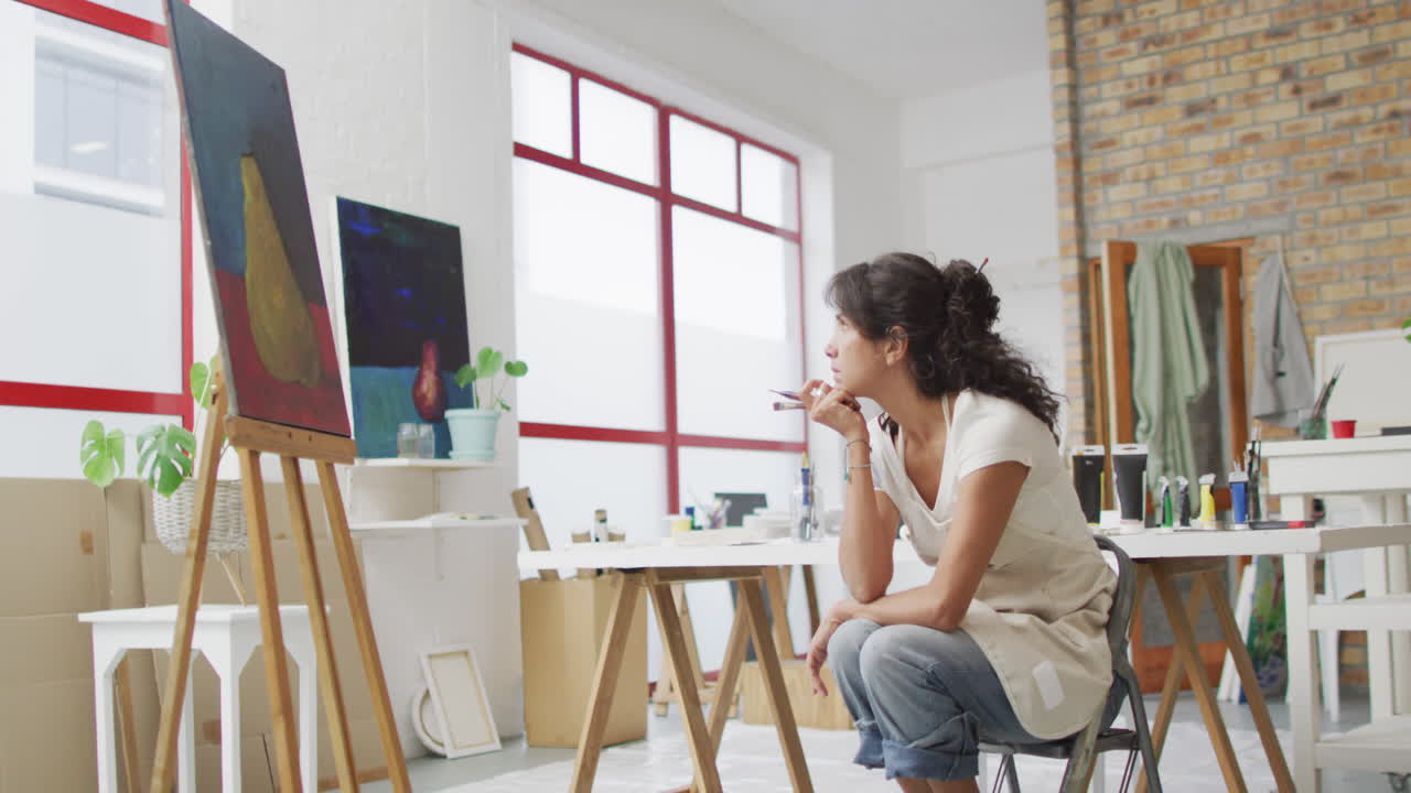 Biracial woman ponders her painting in a bright studio