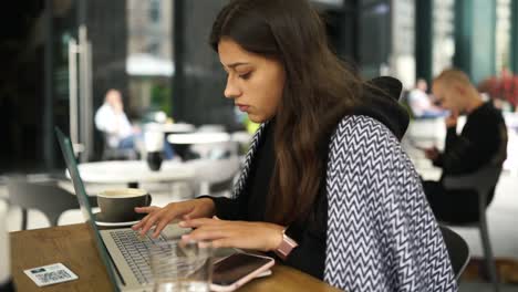 mujer joven trabajando en una computadora portátil en un café