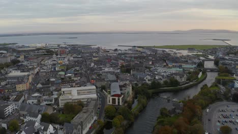 Aerial-descent-shot-of-Galway-City-during-sunset,-featuring-the-River-Corrib