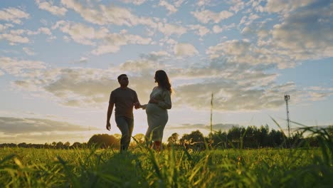 pregnant couple walking in a field at sunset
