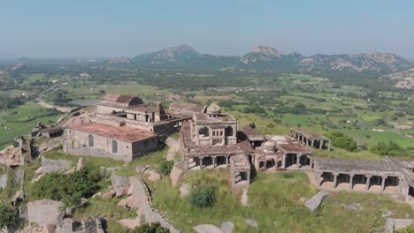 Aerial-orbiting-shot-of-Krishnagiri-Fort-Building-complex-standing-on-green-mountain