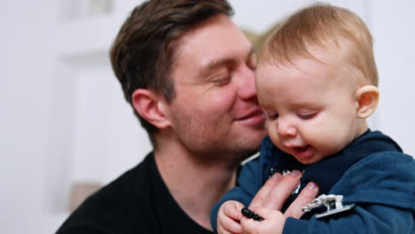 loving caucasian father kisses his cute blond baby boy. smiling infant is playing with bracelet. close up.
