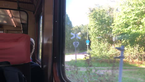 looking through the windows of an old orange train - railcar that are moving, outside the trees passing by