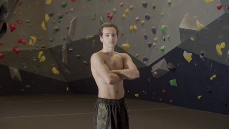 medium shot of a young shirtless sportsman standing in bouldering gym and looking at the camera