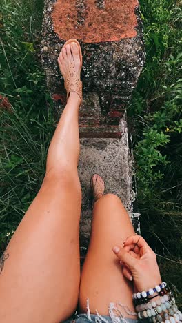 weibliche beine in sandalen und shorts auf einer ziegelsteinkonstruktion