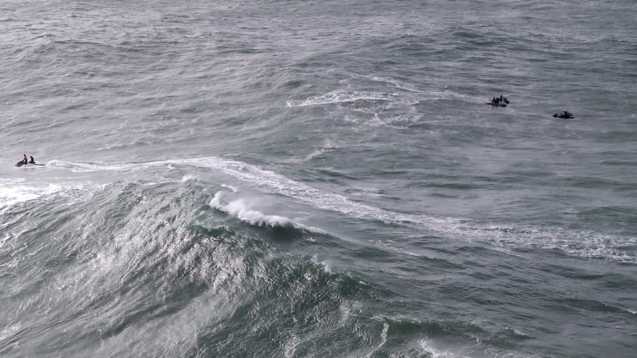 Jet ski riders scanning giant Nazaré wave faces. Portugal, Europe, professional big wave tow-in surfing competition location