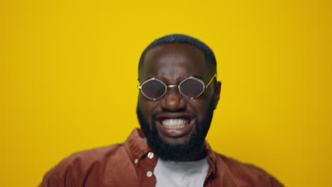 closeup positive african american guy in sunglasses dancing in yellow background