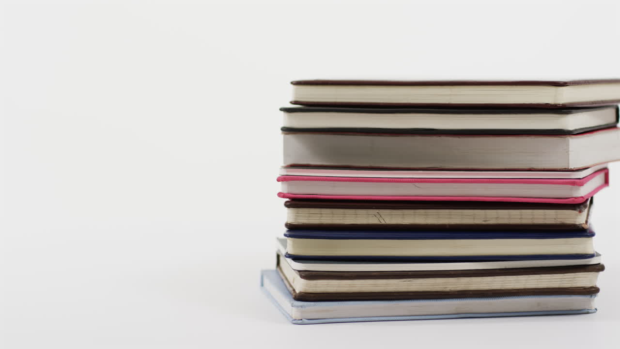 A stack of hardcover books in various colors leans slightly to the side, with copy space