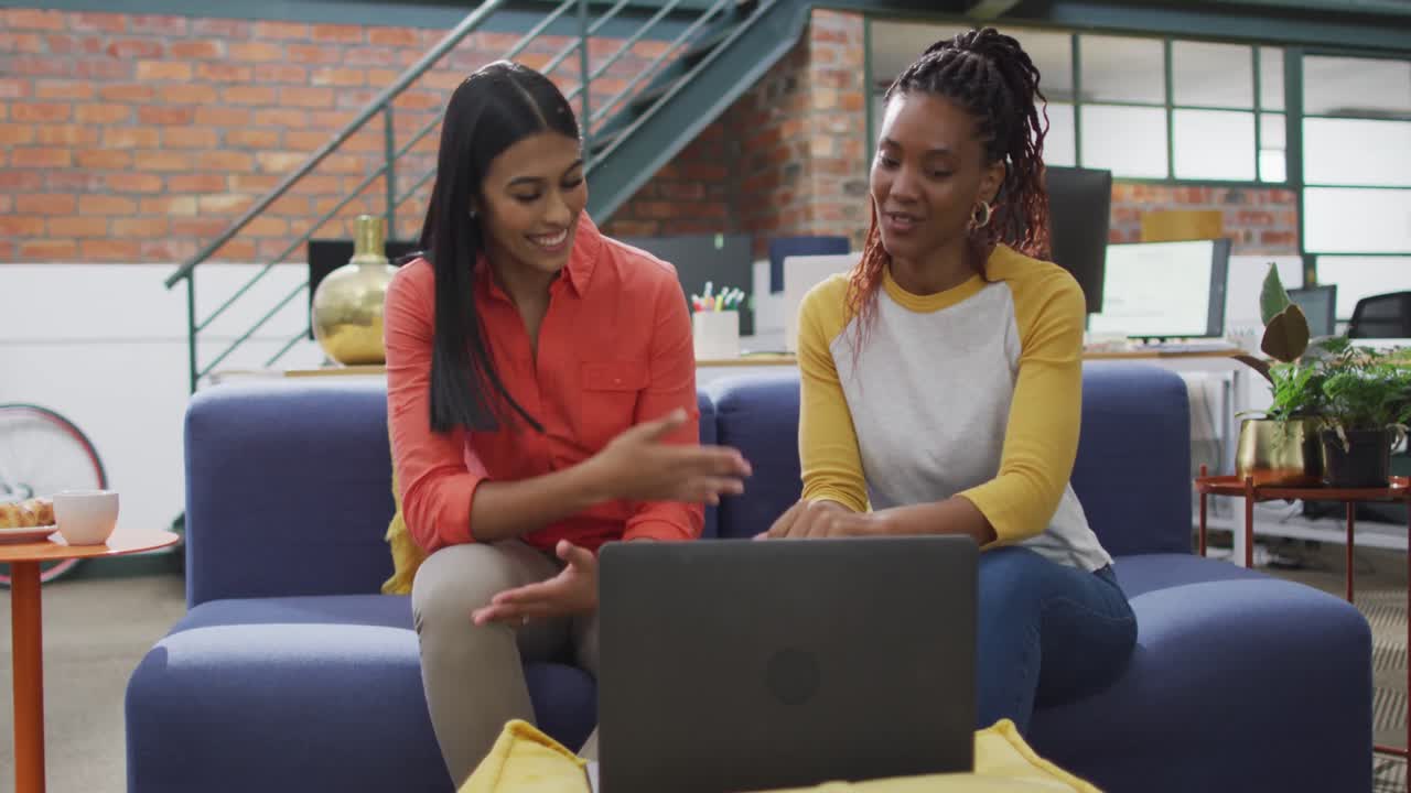 Happy diverse female business colleagues using laptop at office