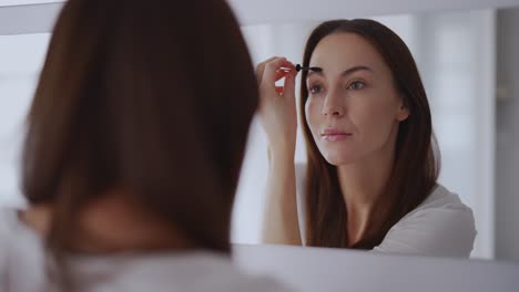 mujer aplicando maquillaje de cejas frente al espejo