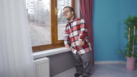hombre enano llorando mirando por la ventana de su casa.