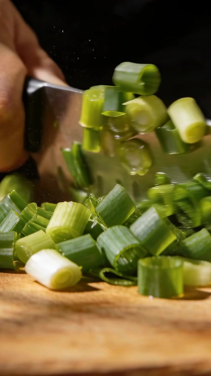 Vídeo vertical: Mão de cozinheiro picando, começando o corte na tábua com faca de chef, fazendo rodelas de cebolinha