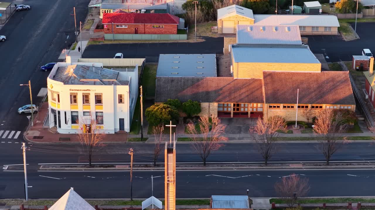 Aerial camera smoothly pans across a quiet town intersection in Coonabarabran, New South Wales, Australia, during early morning golden hour lighting