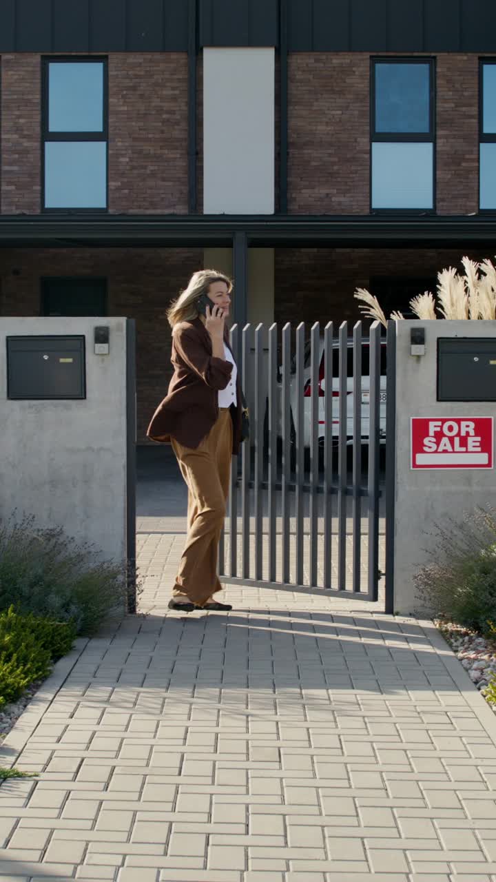 Businesswoman talking on phone outside a house for sale