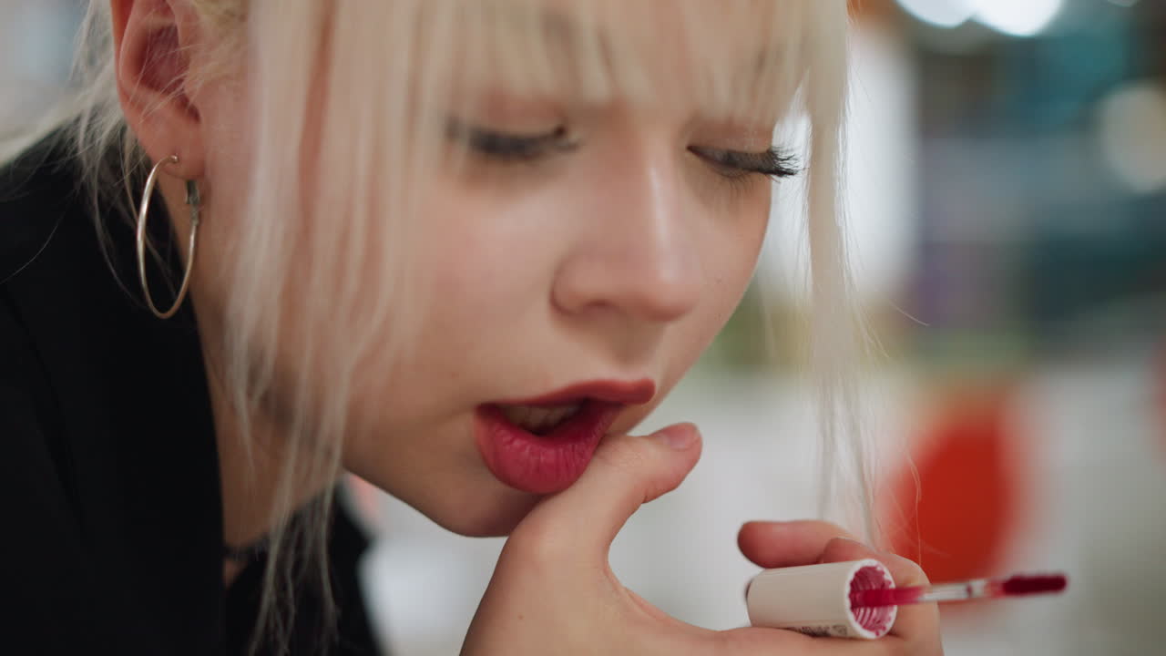 Extreme close up of blonde woman with hoop earrings and soft bangs applying lipstick with delicate focus, lips slightly parted, showing beauty, elegance, and stylish lifestyle routine
