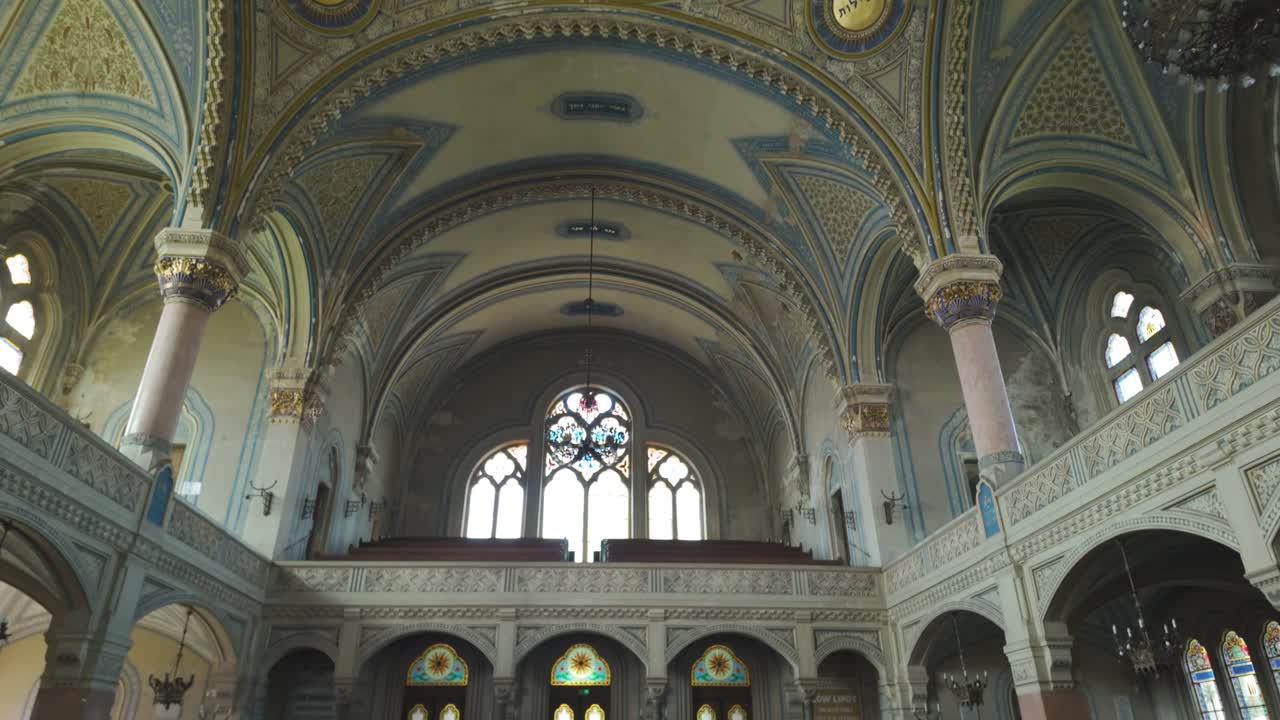 Scenic pan moving from the ornate ceiling toward the seating area inside Szeged Synagogue, capturing architectural elegance