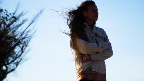 close up silhouette of young woman with long hairs standing on mountaintop during windy day in the evening