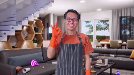 ama de llaves masculina asiática con un delantal mostrando un gesto de ok y sonriendo mientras está de pie en la casa