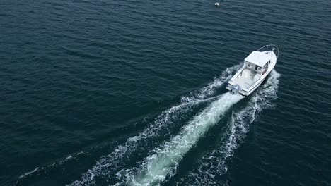 a sisu 22 boat accelerates through boothbay harbor, maine, as a man waves from the deck, enjoying the sunny day on the water