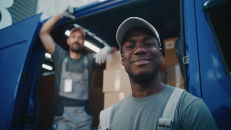 two smiling delivery men stand by their van filled with packages