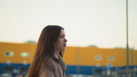 una toma de primer plano de una joven con una chaqueta de melocotón, capturada durante una actividad al aire libre en un parque. la imagen destaca su parte superior del cuerpo y la expresión facial, en un fondo urbano borroso