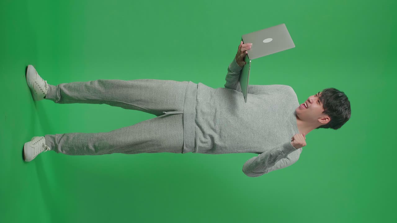 cuerpo lleno de hombre asiático sonriente flexiona el músculo mientras escribe en la computadora en el estudio de pantalla verde