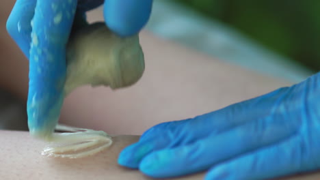 primer plano en el salón de belleza maestro en guantes haciendo el procedimiento para eliminar el vello en las piernas con una mezcla de azúcar