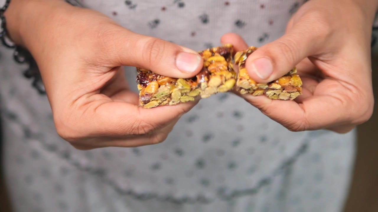 Pessoa Partindo uma Barra de Granola de Nozes e Sementes ao Meio