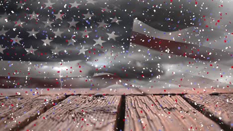 Animation-of-multicolored-falling-confetti-over-wooden-planks-against-flag-of-america-in-cloudy-sky
