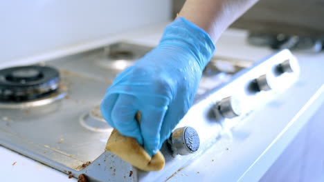 cleaning a stove top in a modern kitchen. person wearing gloves scrubs a dirty stove top, removing grease and crumbs in a bright kitchen environment
