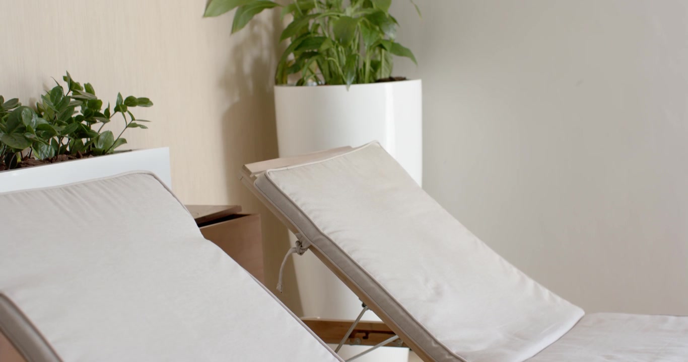 Camera panning right and upward in spa lounge, revealing two recliners and planter