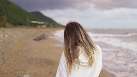back-view-portrait-of-blonde-woman-walking-along-ocean-coast,-talking-by-phone