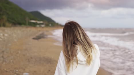 back view portrait of blonde woman walking along ocean coast, talking by phone