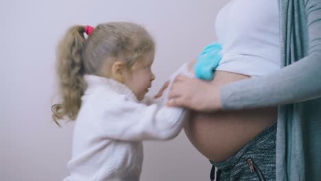 niña pisando el estómago de una mamá embarazada con botas azules divertidas