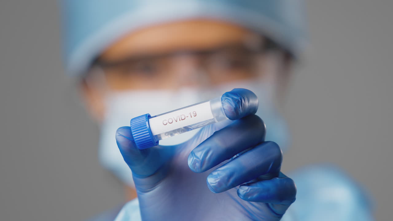 primer plano de una trabajadora de investigación de laboratorio que lleva un ppe con un tubo de ensayo etiquetado con covid-19