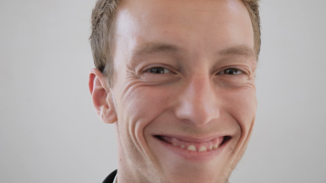 Rosto masculino caucasiano sorrindo, de óculos, olhando para a câmera