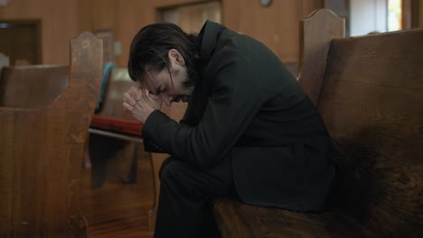 Young-man-in-black-suit-praying-in-church-pew-in-cinematic-slow-motion-with-folded-hands