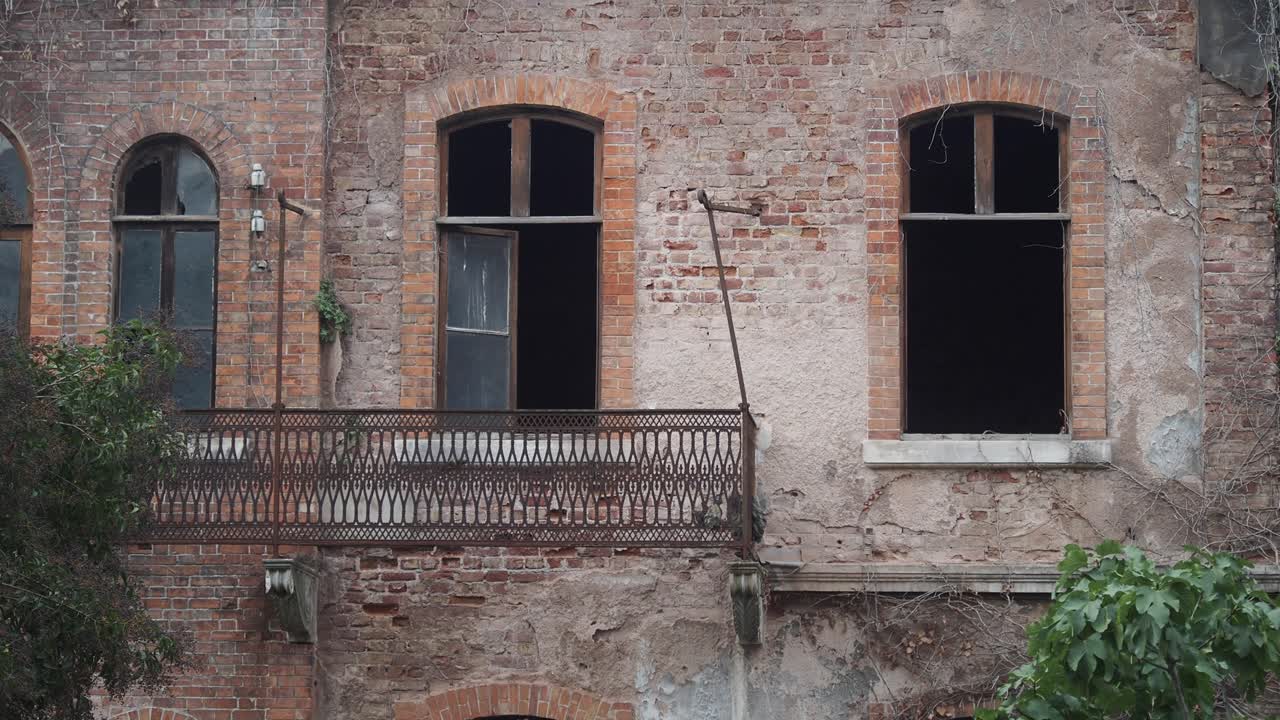Edificio in mattoni fatiscente con finestre ad arco e balcone arrugginito