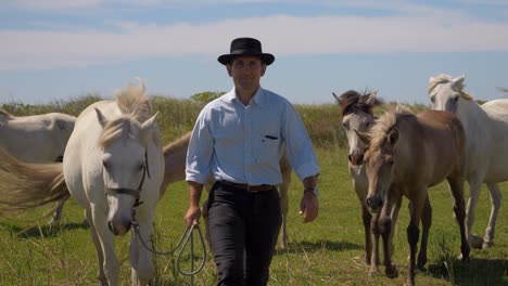 cowboy taking the leader of the horse herd and walking away with her and then the whole herd follows