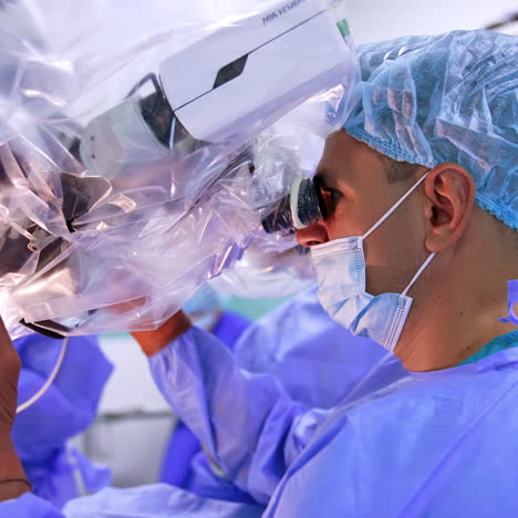 confident male doctor in mask and cap looks attentively at microscope. surgeon adjusts the equipment and applies tools. side view.