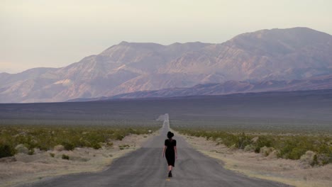 Woman-walking-on-road-towards-beautiful-mountain-in-Death-Valley-National-Park-in-California,-USA