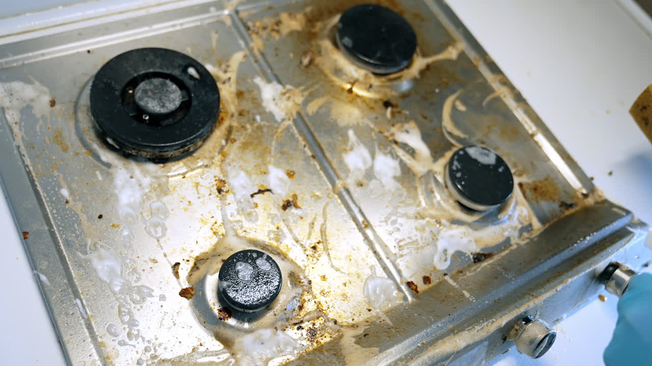 Cleaning a dirty stovetop in the kitchen. A person uses a sponge to scrub a stained stovetop in a kitchen, removing grease and food residue effectively