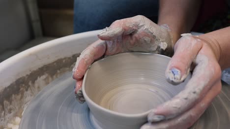 Young-woman-artist-making-clay-bowl-on-pottery-wheel