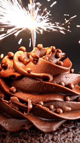 three chocolate cupcakes with chocolate frosting and sprinkles on top. one of the cupcakes has a lit sparkler on top