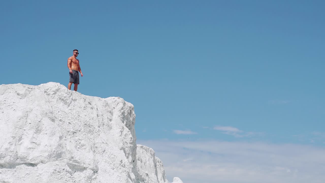 The winner man runs to the top of the mountain. A shirtless bodybuilder stands on a mountain against a blue sky