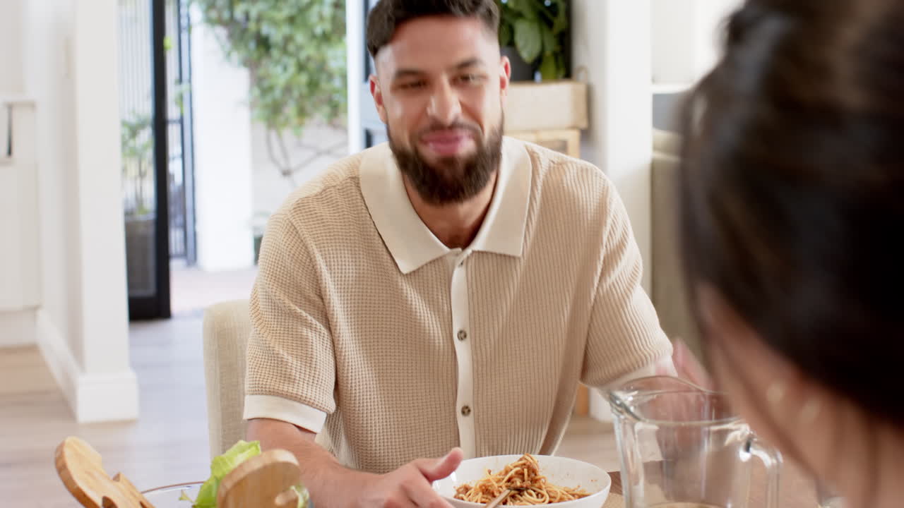 Smiling man enjoying meal with friend at dining table, having conversation
