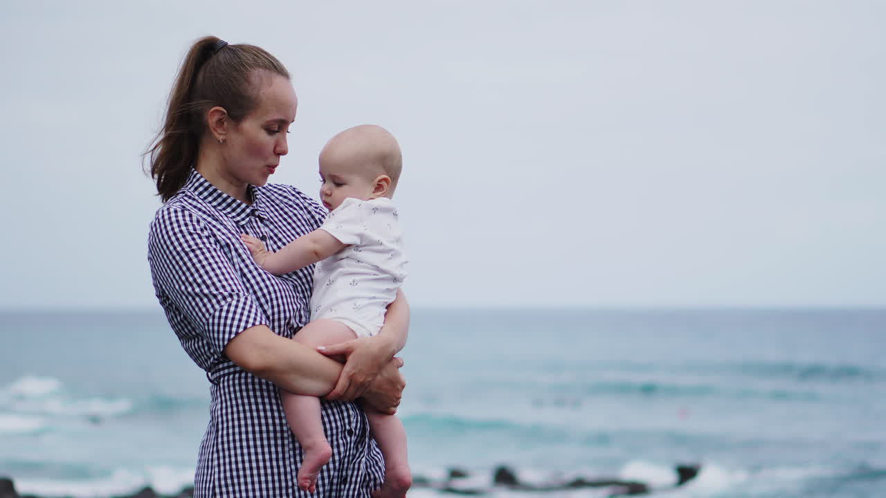 Amid the sea and beach scenery, a beautiful portrait showcases a mother's affectionate kiss for her daughter. The backdrop reflects a happy family on vacation, with the mom hugging her toddler